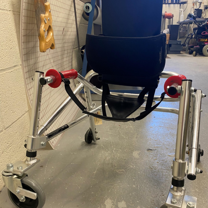 Training device for walking with black straps for support, oversized red handles, 4 wheels, and metal rods