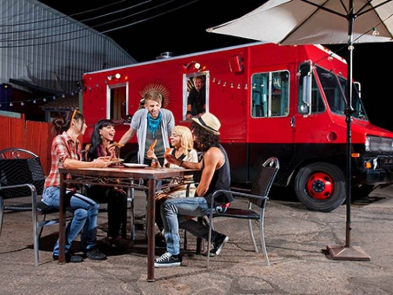 A group of friends at a table in front of a red mobile food truck