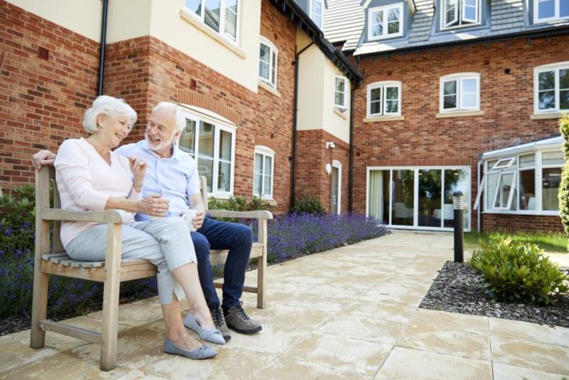 Elderly couple seated on a bench outside a building.