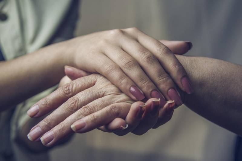 Young person's hands holding an elderly person's hands to comfort them. 