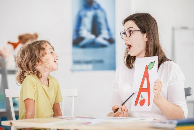 A young woman is holding a flashcard for a young child to read. 