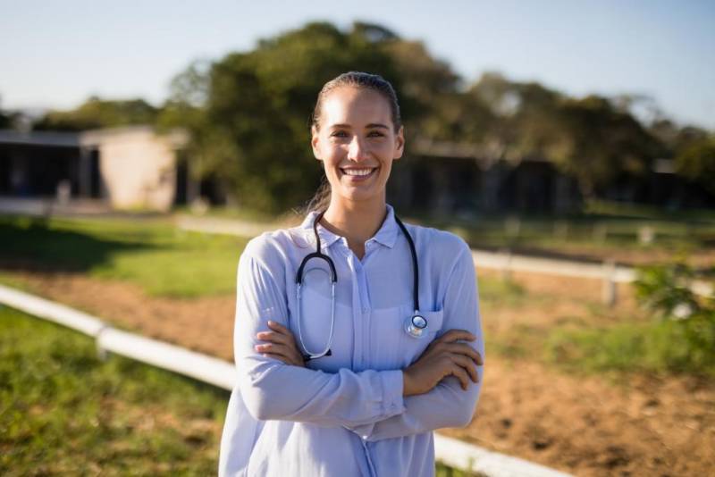 Young nurse smiling outside a rural hospital setting.