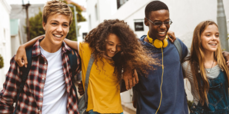 Group of smiling teens, 2 male and 2 female, smiling as they walk together