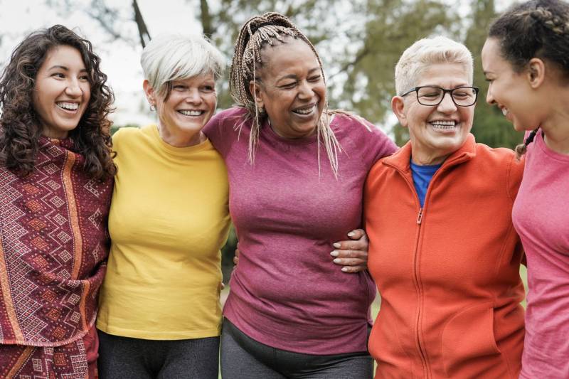 Five smiling women arms around each other