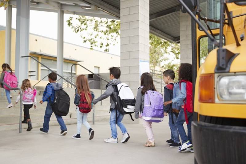 Line of young students getting off school bus and entering school