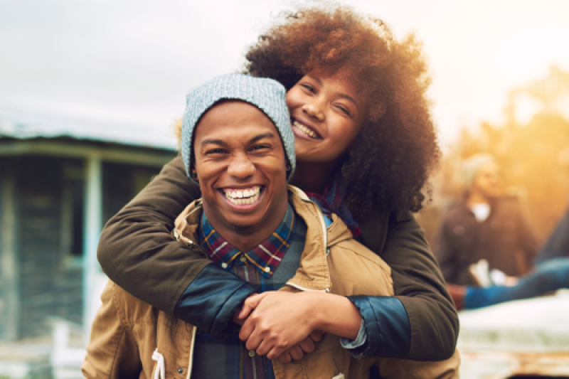 Image of a man smiling and a woman with her arms around his shoulders