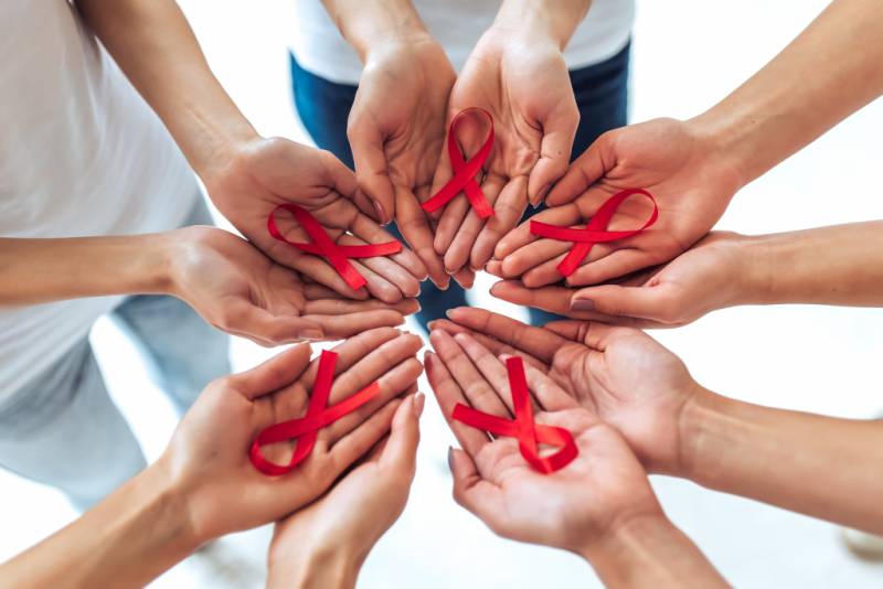 Hands in a circle each holding red ribbon