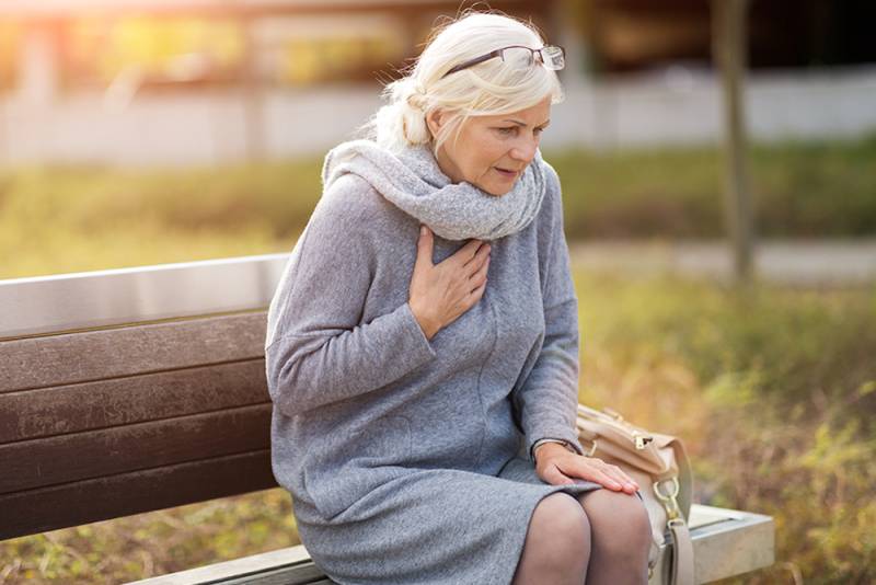 Senior Woman Suffering From Chest Pain While Sitting On Bench