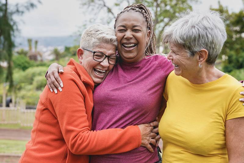 Happy multiracial senior women having fun together at park - Elderly generation people hugging each other outdoor
