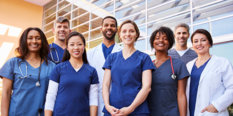 A group of various health care providers standing in front of a medical facility.