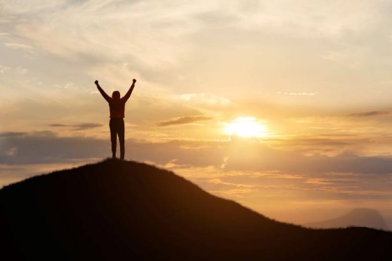 A person stands at the top of a mountain in victory