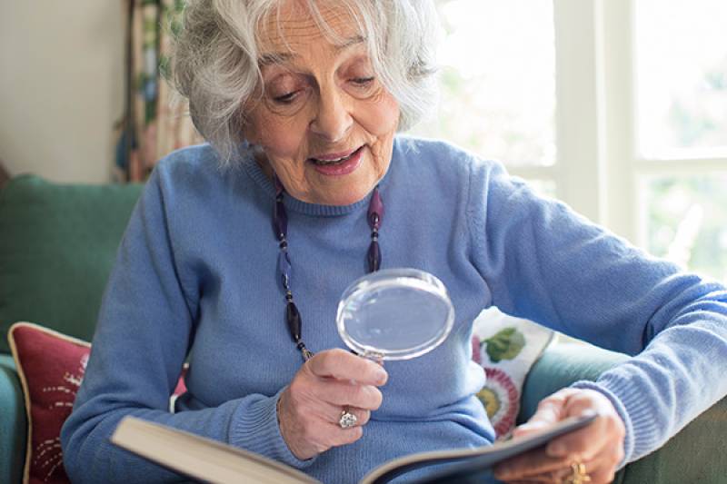 Senior woman sitting in a chair using a magnifier to read.