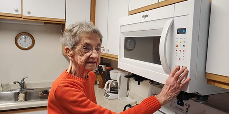 Older woman with low vision using bump dots to operate her microwave. 