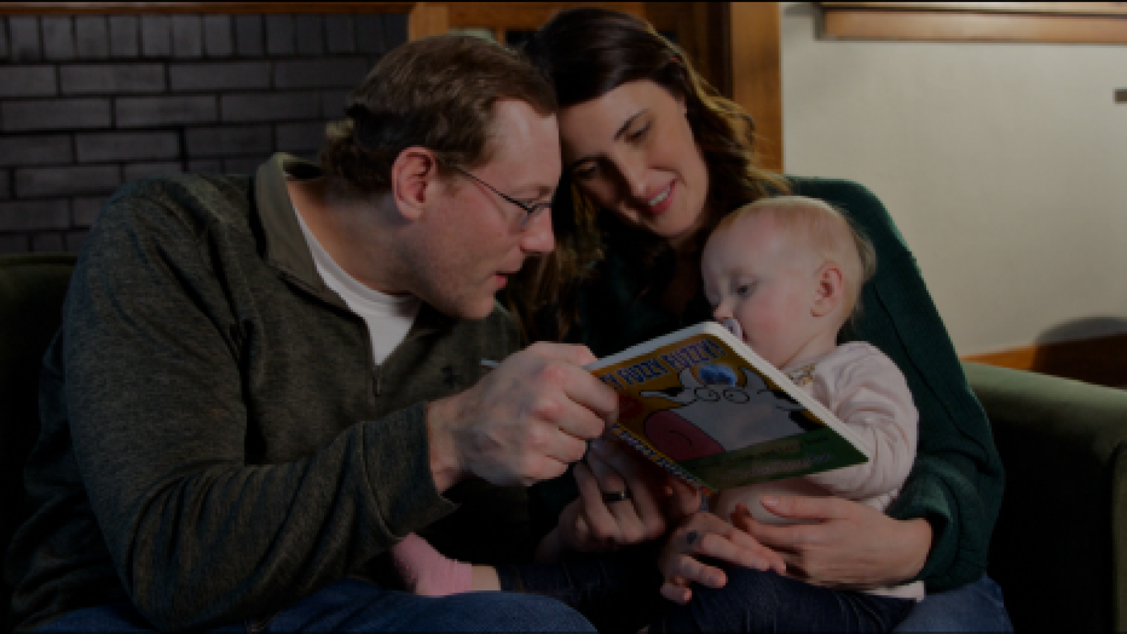 Father reading a book to his baby while the mother holds him
