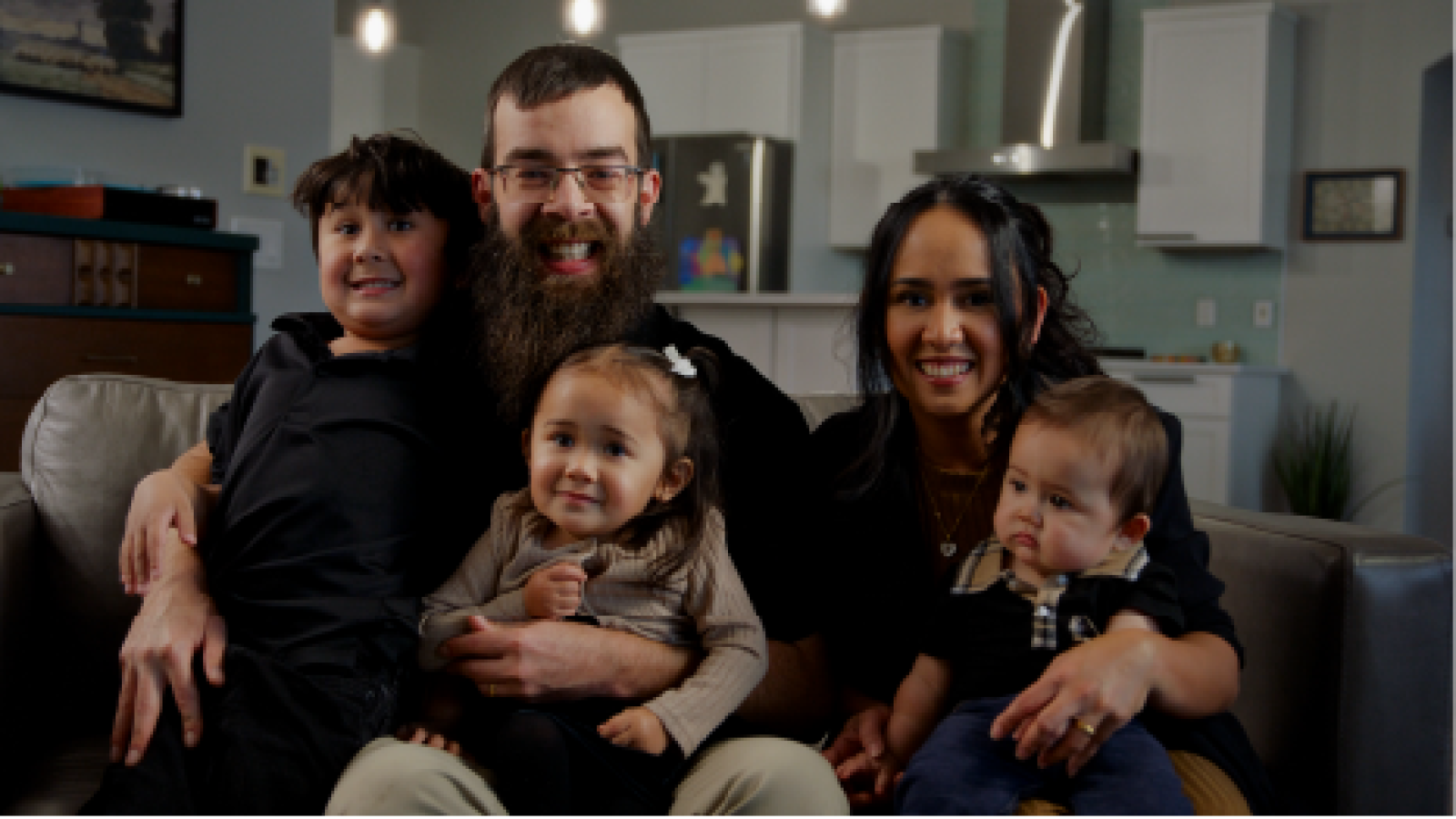 father and mother sitting on couch with their three children