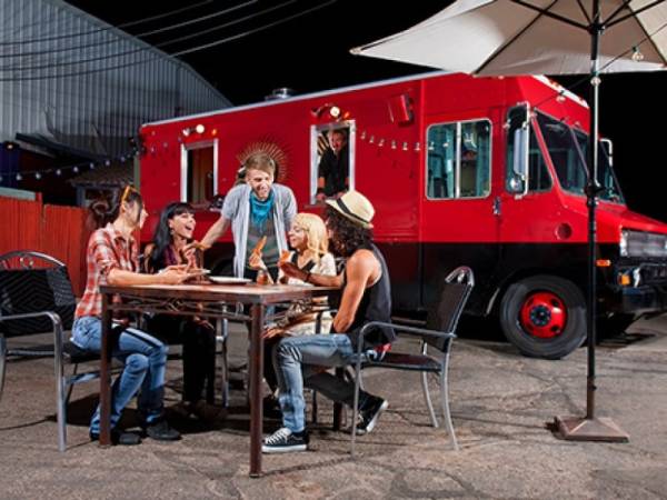 A group of people at a table in front of a red mobile food truck.