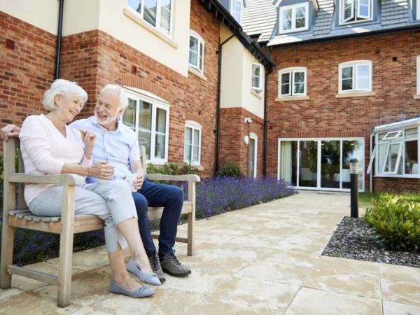 Elderly couple seated on a bench outside a building.