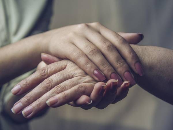 Young person's hands holding an elderly person's hands to comfort them. 