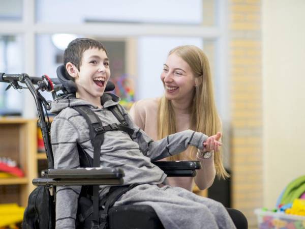 Young boy in a wheelchair with and adult smiling at his side. 