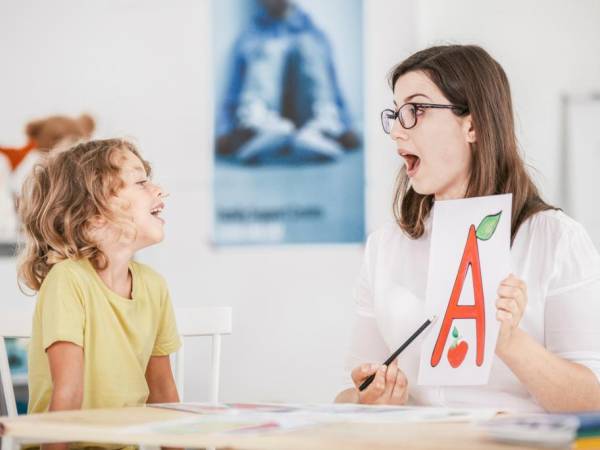 A young woman is holding a flashcard for a young child to read. 