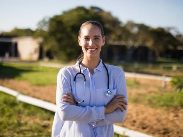 Young nurse smiling outside a rural hospital setting.
