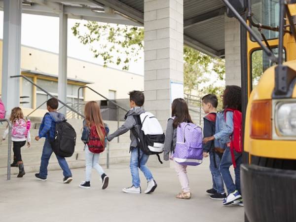 Line of young students getting off school bus and entering school