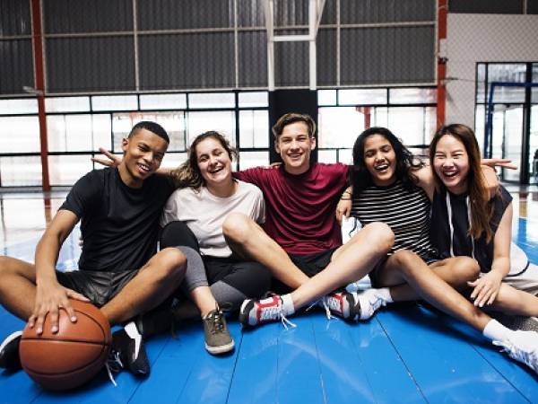 Group of five teens sitting in gym floor with basketball