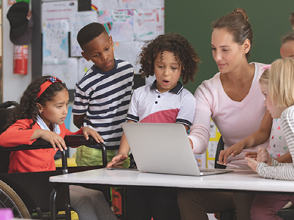 A teacher shows a group of students something on her laptop