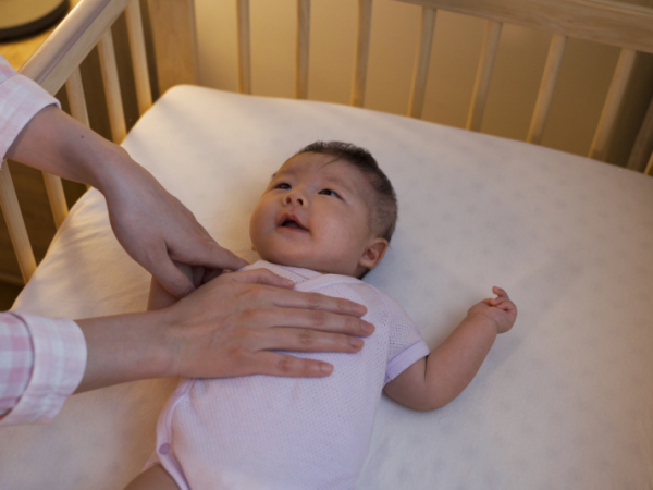 Hands reaching in to check on baby in a crib