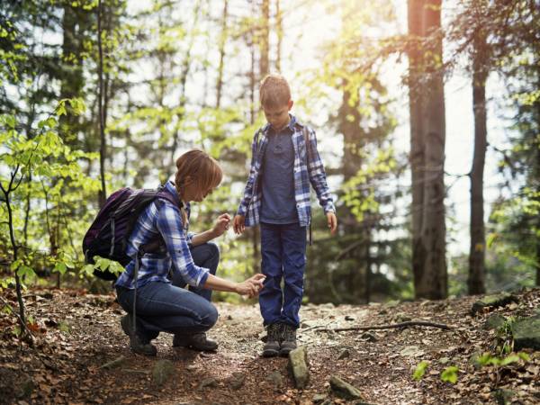Mother spraying her son with insect repellent while outside hiking on trail
