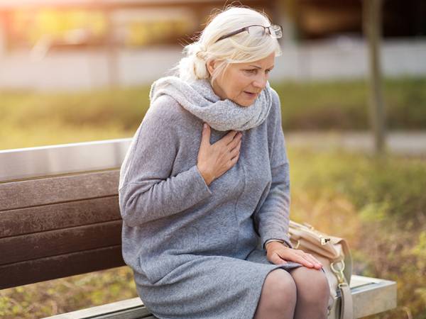 Senior Woman Suffering From Chest Pain While Sitting On Bench