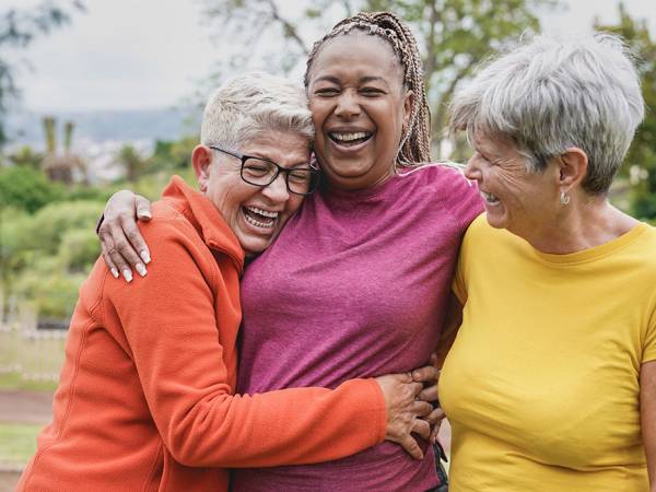 Happy multiracial senior women having fun together at park - Elderly generation people hugging each other outdoor