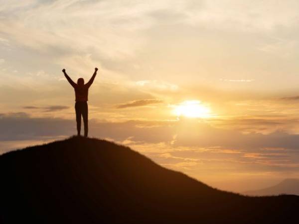 A person stands at the top of a mountain in victory