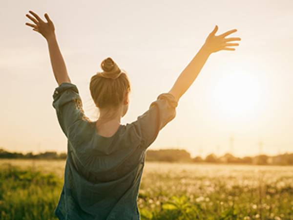 Woman raising hands with sunset in background