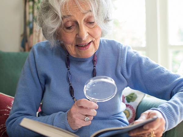 Senior woman sitting in a chair using a magnifier to read.