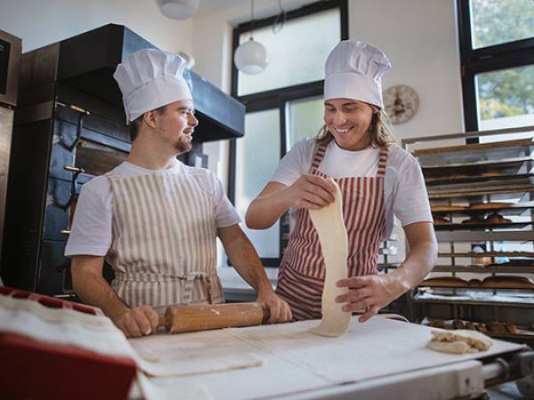 Male in a bakery show a man with down syndrome how to prepare bread.