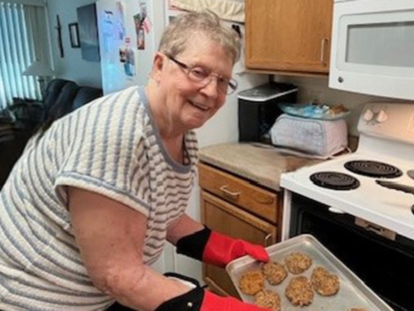 Older woman with short gray hair and wearing glasses getting cookies out of the oven.