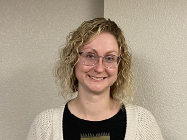 A female with medium length curly blonde hair, wearing glasses, black shirt, beige cardigan, and holding an award.