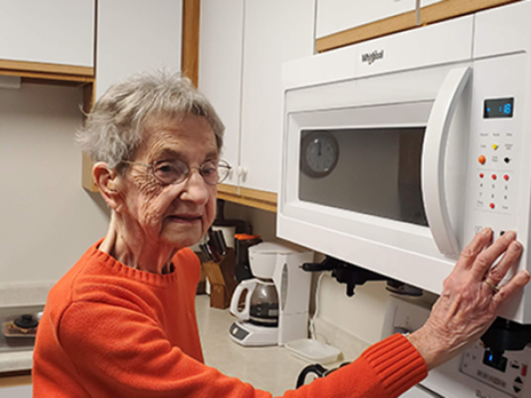 Older woman with low vision using bump dots to operate her microwave. 