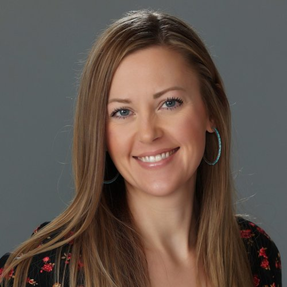 Headshot of a woman with long brown hair and blue eyes smiling. Wearing a black and red blouse and hoop earrings.