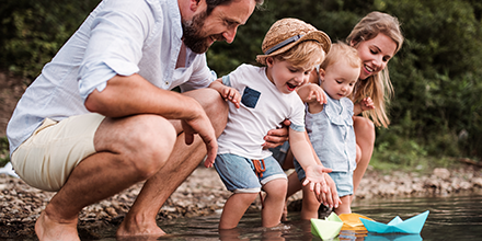 a family of four playing with paper boats in a creek