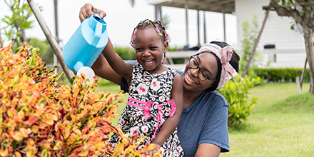a smiling mother helping her daughter water flowers