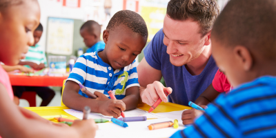 three children coloring at table with teacher