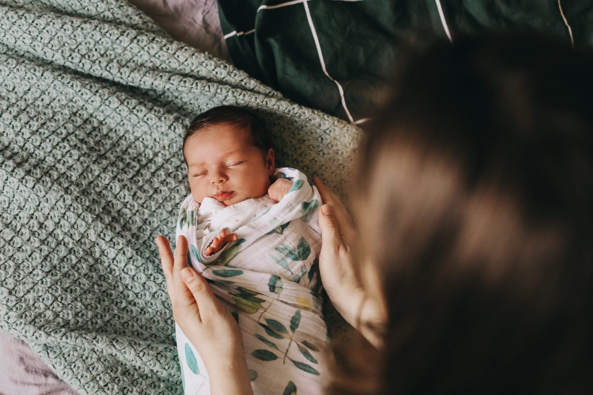 A young mother swaddling a newborn baby.