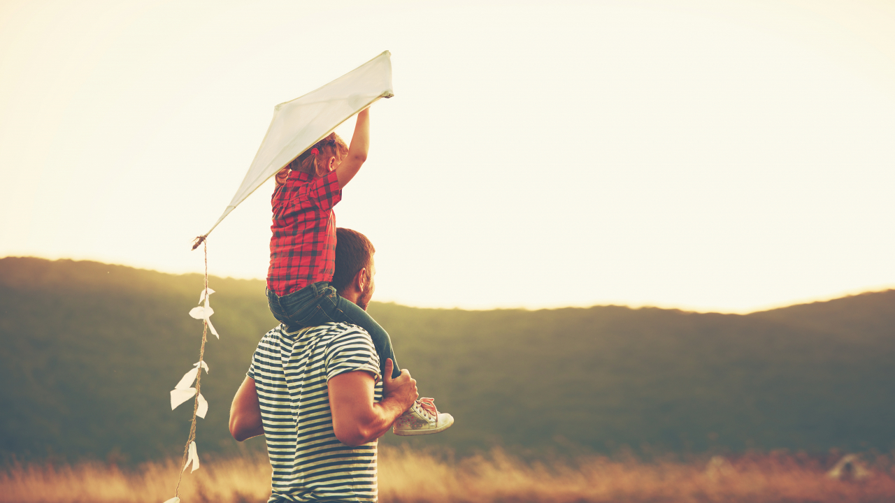 Child sitting on fathers shoulder flying kite