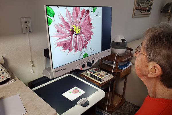 Woman using a video magnifier to paint a card.