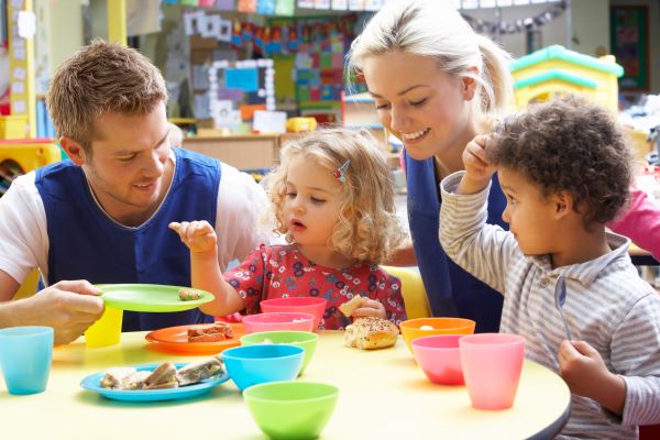 two children playing at table with childcare staff