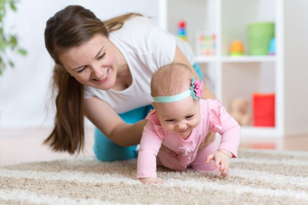 woman helping infant girl crawl on the floor