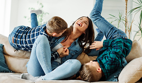 Mother roughhousing on sofa with two young sons