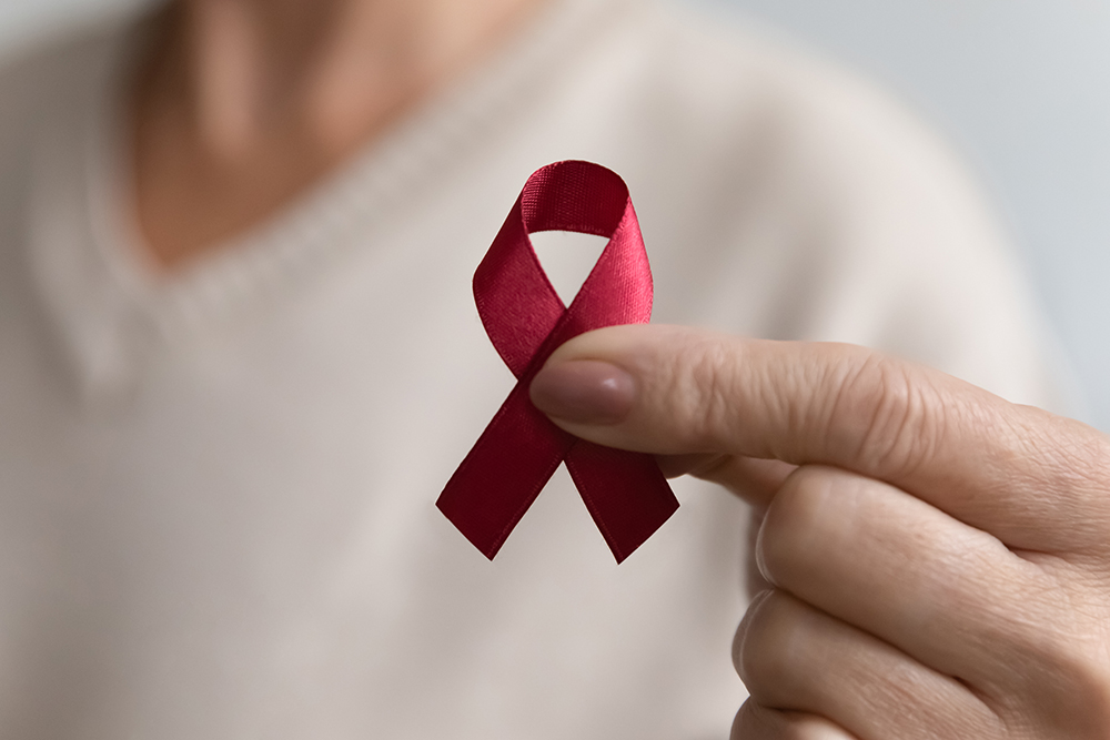 Lady showing hiv or aids awareness symbol, volunteering for charity campaign for prevention immunity disease, cancer, elderly healthcare support. Hand of mature woman holding red ribbon. Close up